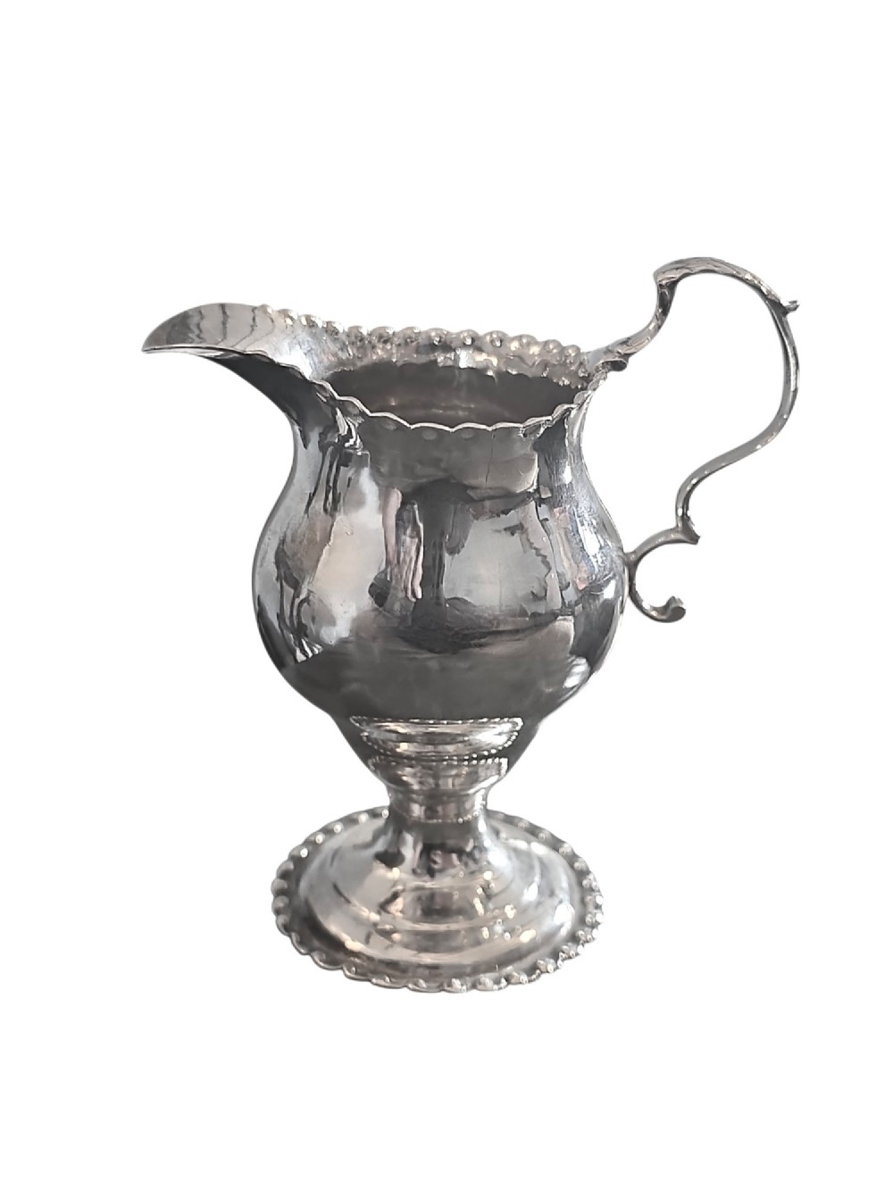 A George III sterling silver cream jug featuring a baluster shape, scalloped rim, double-scroll handle, and pedestal base. View IV