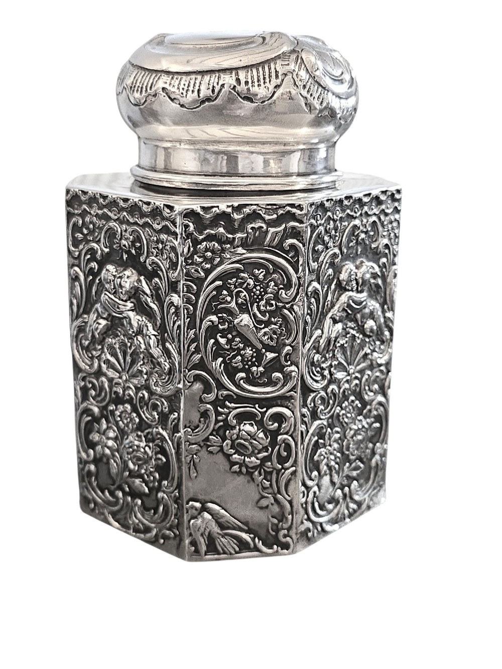 A late Victorian hexagonal sterling silver tea caddy featuring relief repousse work of cherubs, scrollwork, and floral motifs with a fitted domed lid. View III