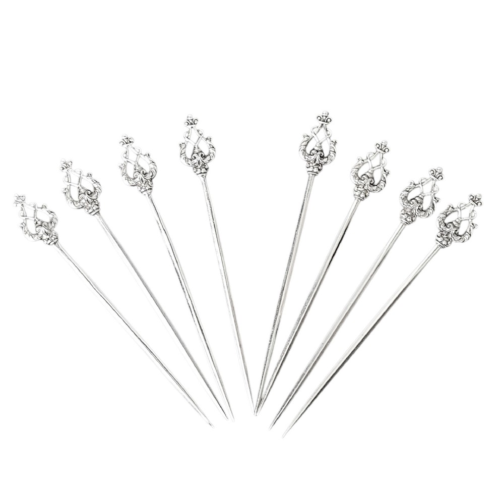 A set of eight sterling silver hors doeuvre skewers arranged in a fan shape, featuring ornate openwork scrollwork handles and tapered pins. View IV