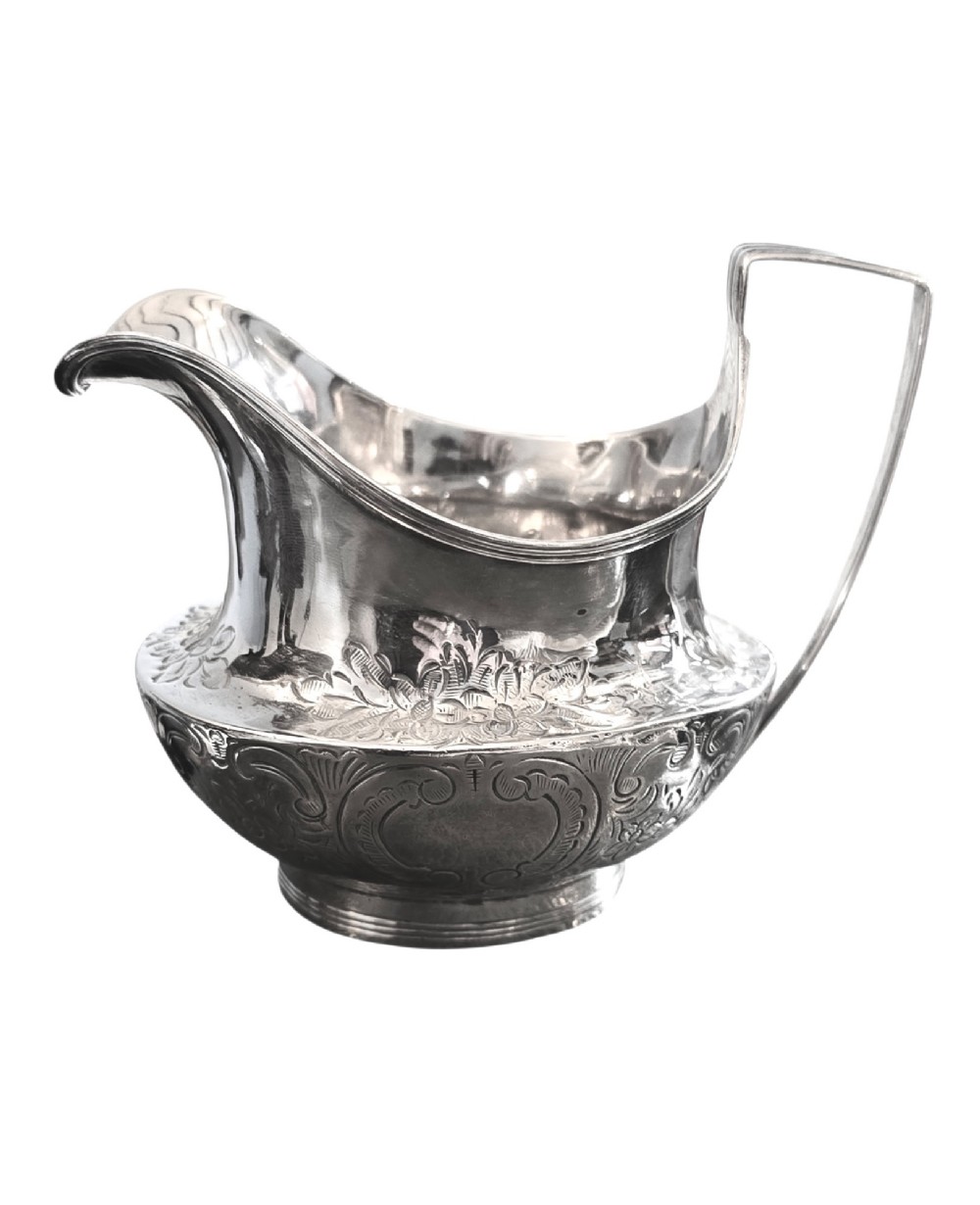 A George III sterling silver cream jug with chased scroll decoration, an angular high loop handle, and a circular foot.