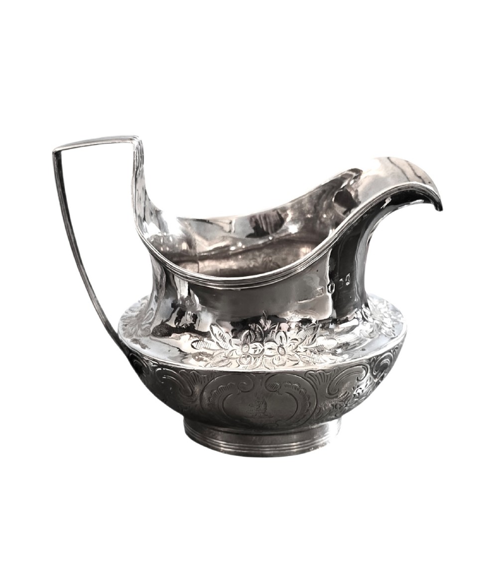 A George III sterling silver cream jug with chased scroll decoration, an angular high loop handle, and a circular foot. View III