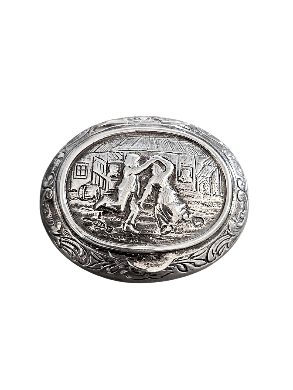 An oval antique sterling silver snuff box featuring an embossed central scene of dancing figures, framed by scrollwork borders.
