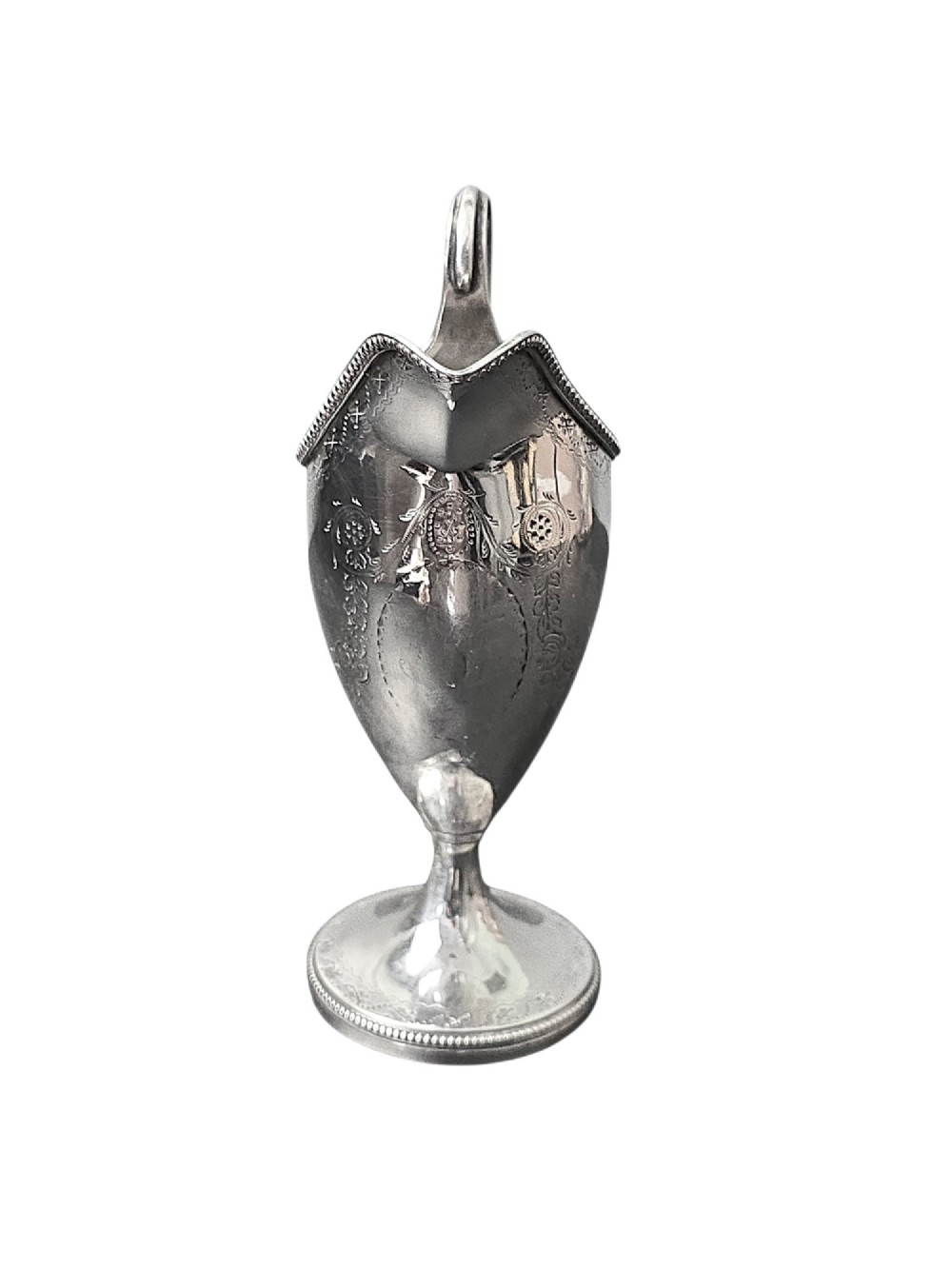 A George III sterling silver helmet-shaped cream jug with bright-cut floral engraving, a beaded rim, a high loop handle, and a circular pedestal foot. View II