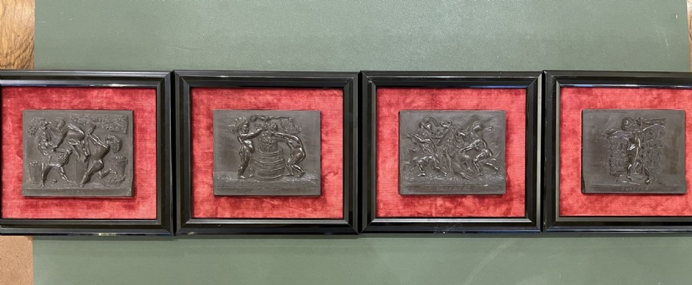 A set of framed hand-carved dark Welsh slate relief plaques mounted against red fabric backgrounds within black moulded frames.