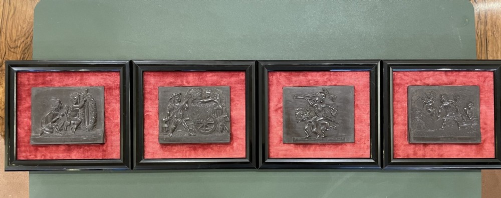 A set of framed hand-carved dark Welsh slate relief plaques mounted against red fabric backgrounds within black moulded frames. View II