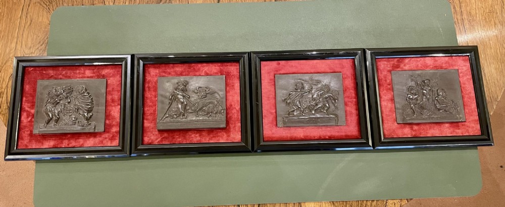 A set of framed hand-carved dark Welsh slate relief plaques mounted against red fabric backgrounds within black moulded frames. View III