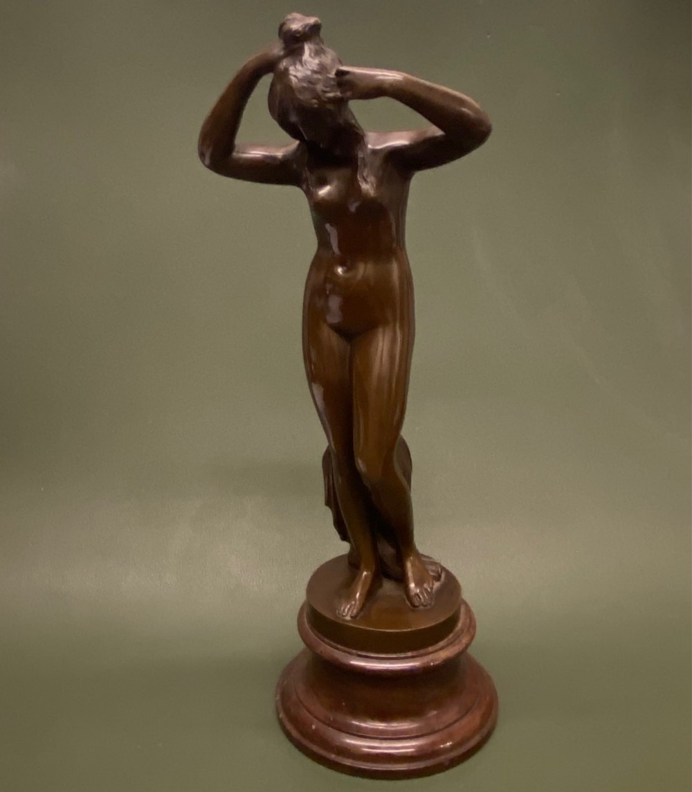 A 19th-century dark brown bronze sculpture of a standing nude female bather wringing her hair, mounted on a tiered circular base.