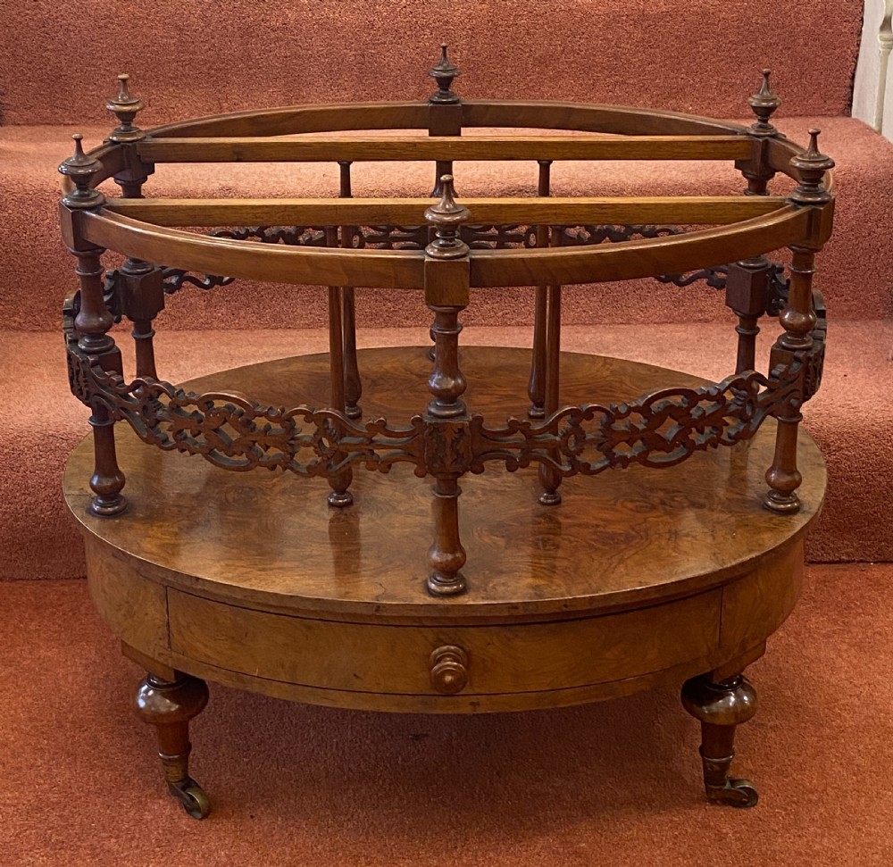 An oval Victorian walnut music canterbury featuring three upper compartments, turned finials, pierced fretwork, a single lower drawer, turned legs, and brass castors.