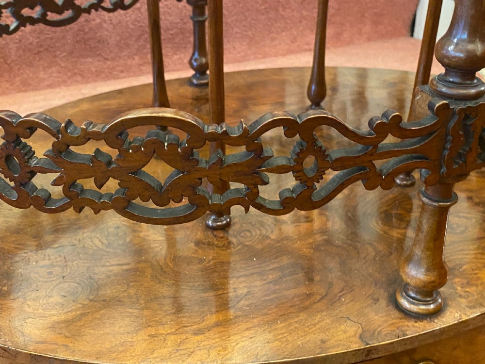 An oval Victorian walnut music canterbury featuring three upper compartments, turned finials, pierced fretwork, a single lower drawer, turned legs, and brass castors. View IV