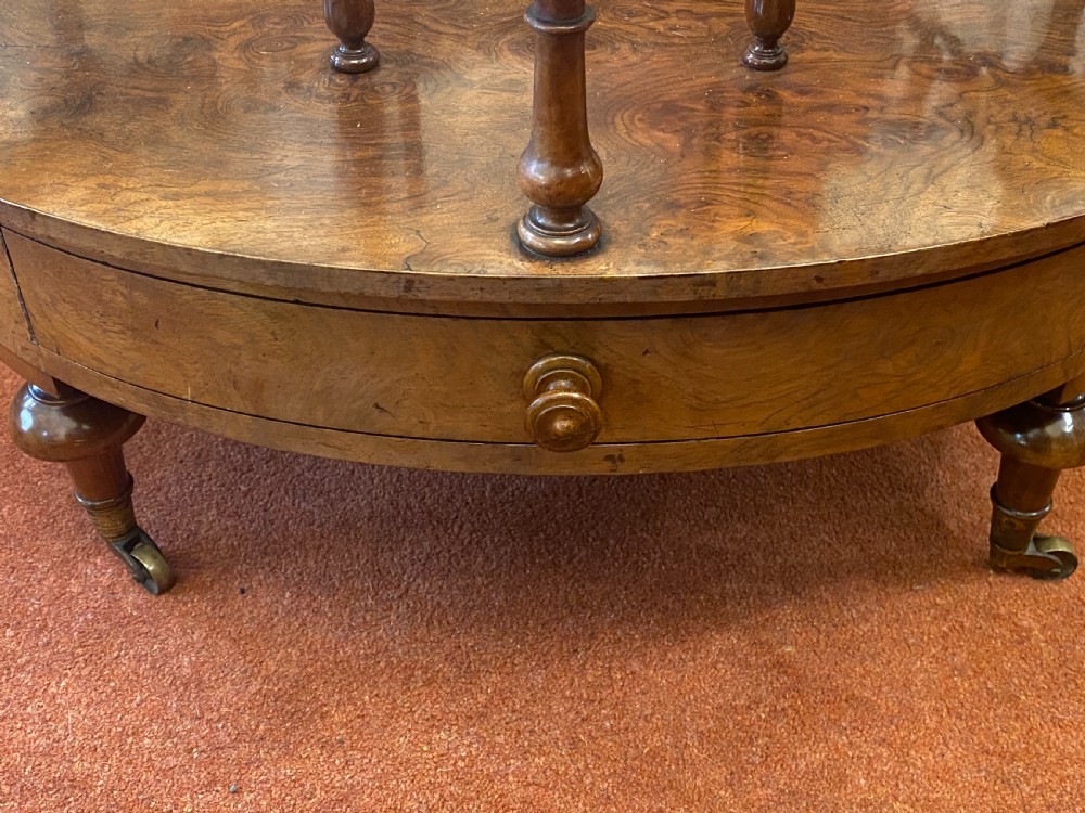 An oval Victorian walnut music canterbury featuring three upper compartments, turned finials, pierced fretwork, a single lower drawer, turned legs, and brass castors. View VI