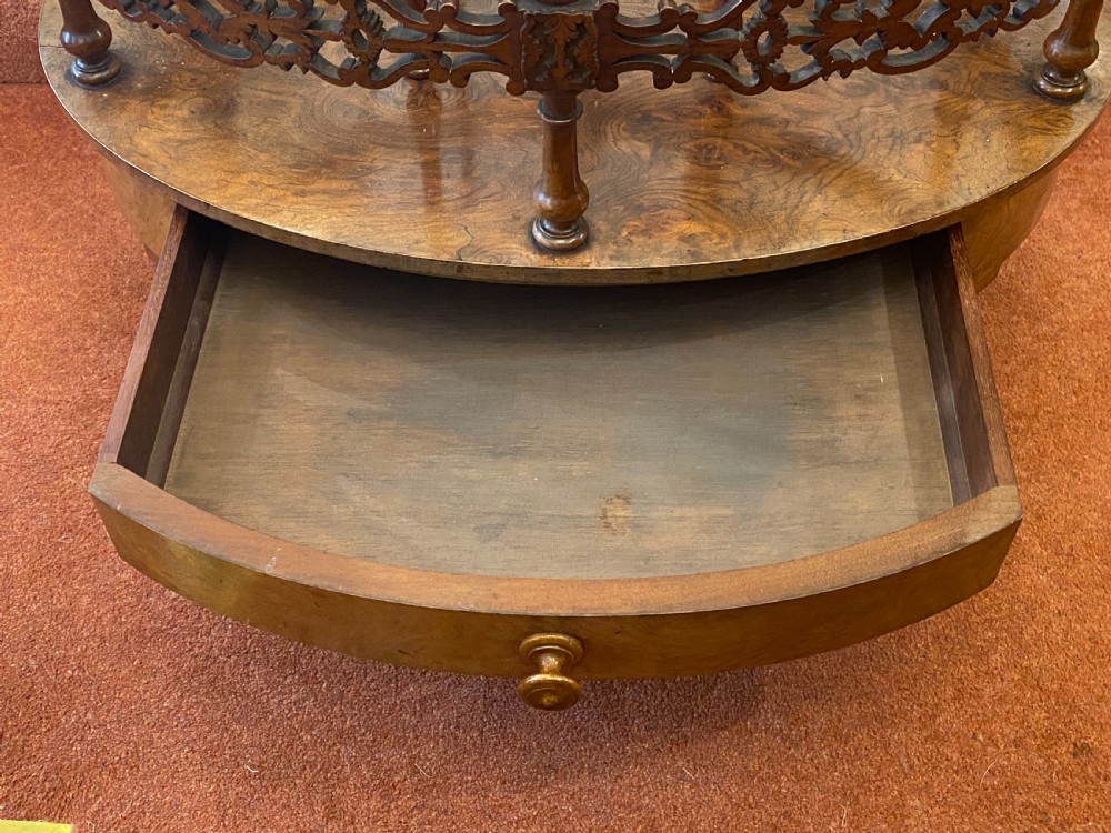 An oval Victorian walnut music canterbury featuring three upper compartments, turned finials, pierced fretwork, a single lower drawer, turned legs, and brass castors. View VII