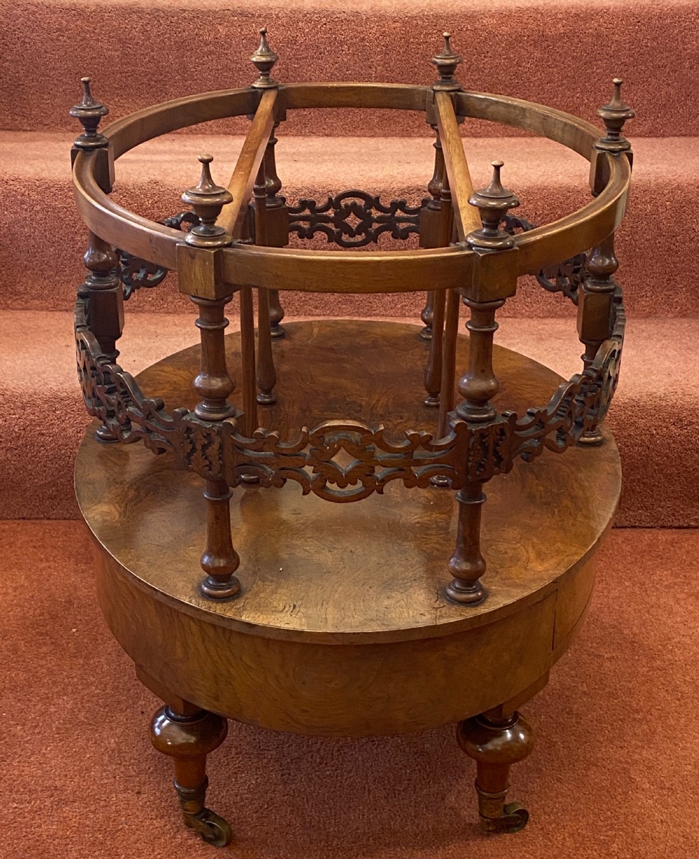 An oval Victorian walnut music canterbury featuring three upper compartments, turned finials, pierced fretwork, a single lower drawer, turned legs, and brass castors. View XIV