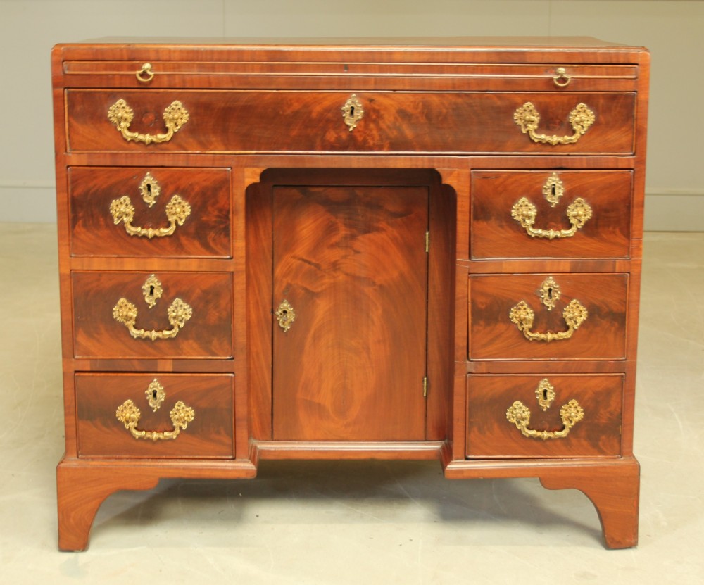 A George III mahogany kneehole desk featuring a top drawer, six side drawers, a central recessed cupboard, and decorative brass handles.