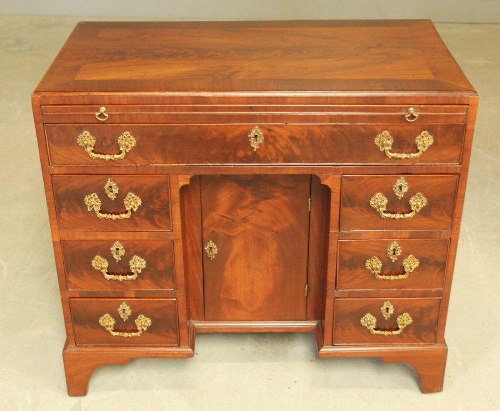 A George III mahogany kneehole desk featuring a top drawer, six side drawers, a central recessed cupboard, and decorative brass handles. View II