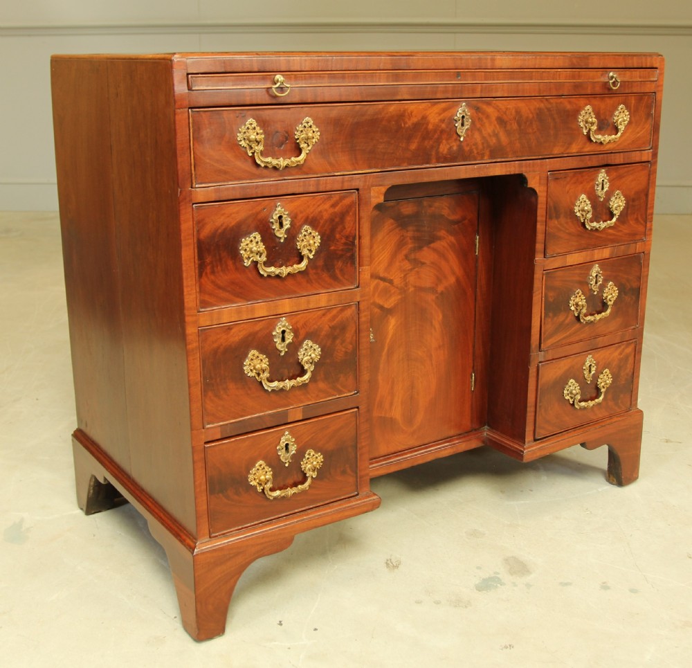 A George III mahogany kneehole desk featuring a top drawer, six side drawers, a central recessed cupboard, and decorative brass handles. View III
