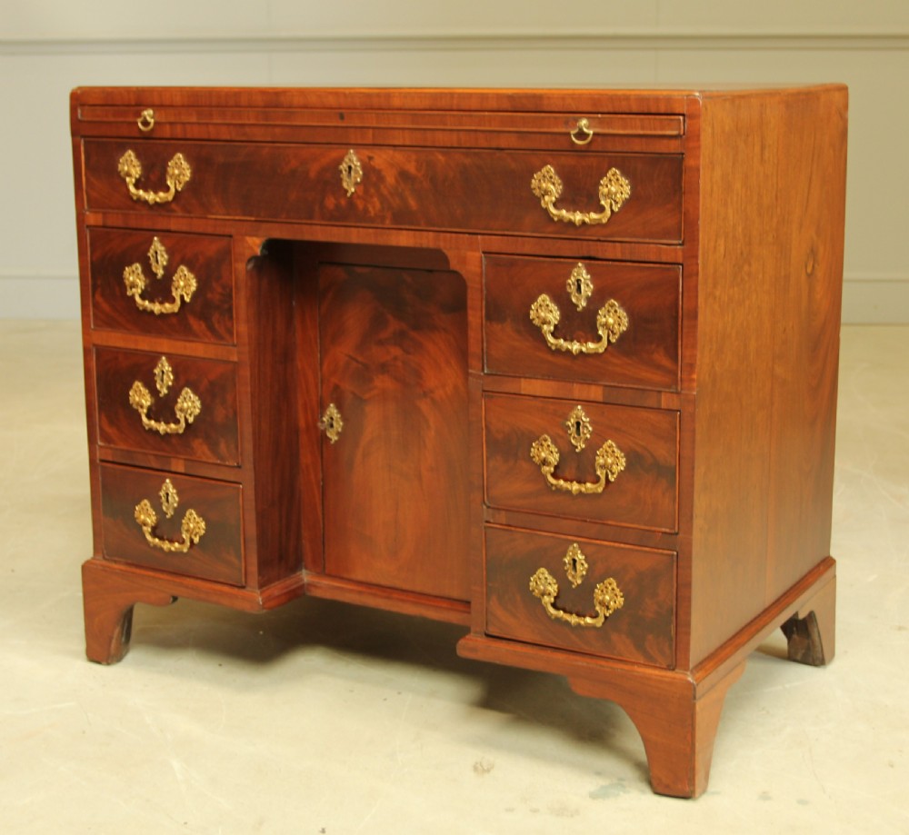 A George III mahogany kneehole desk featuring a top drawer, six side drawers, a central recessed cupboard, and decorative brass handles. View V