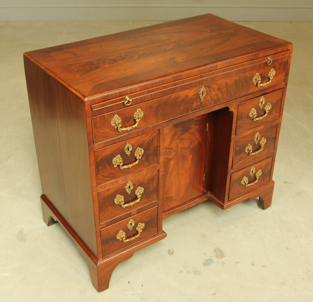 A George III mahogany kneehole desk featuring a top drawer, six side drawers, a central recessed cupboard, and decorative brass handles. View VI