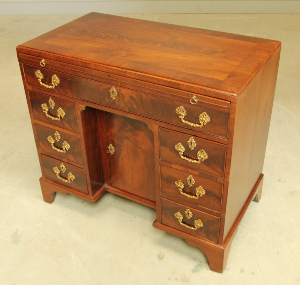 A George III mahogany kneehole desk featuring a top drawer, six side drawers, a central recessed cupboard, and decorative brass handles. View VII