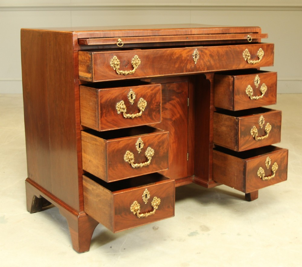 A George III mahogany kneehole desk featuring a top drawer, six side drawers, a central recessed cupboard, and decorative brass handles. View VIII