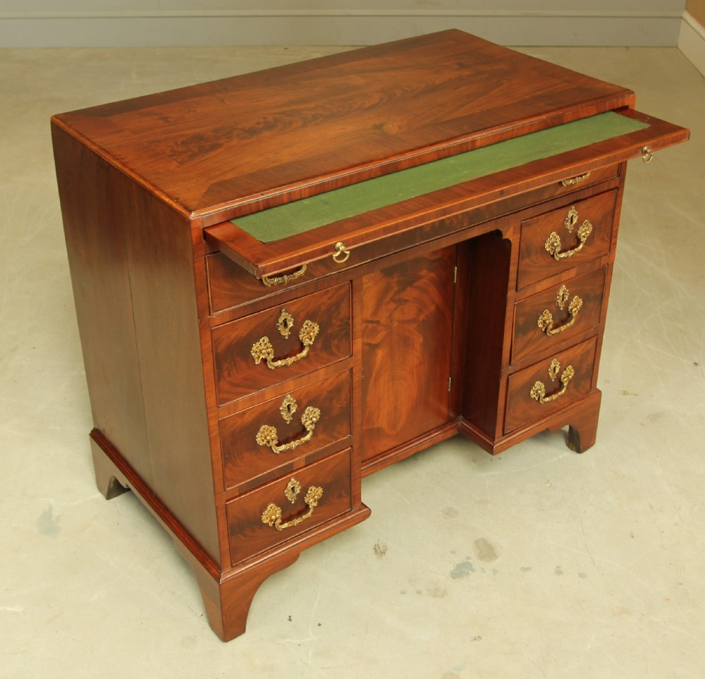 A George III mahogany kneehole desk featuring a top drawer, six side drawers, a central recessed cupboard, and decorative brass handles. View IX
