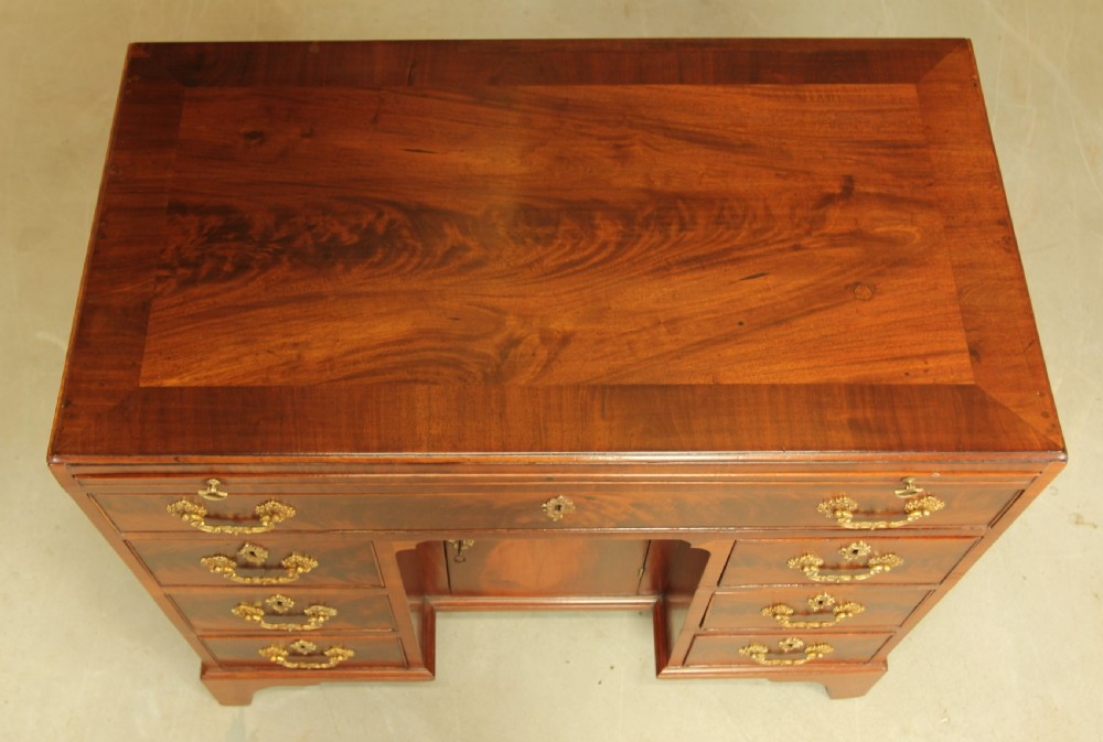 A George III mahogany kneehole desk featuring a top drawer, six side drawers, a central recessed cupboard, and decorative brass handles. View X