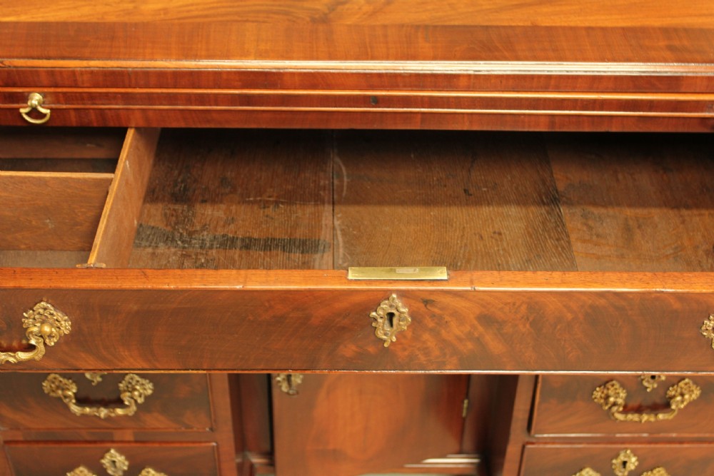 A George III mahogany kneehole desk featuring a top drawer, six side drawers, a central recessed cupboard, and decorative brass handles. View XI