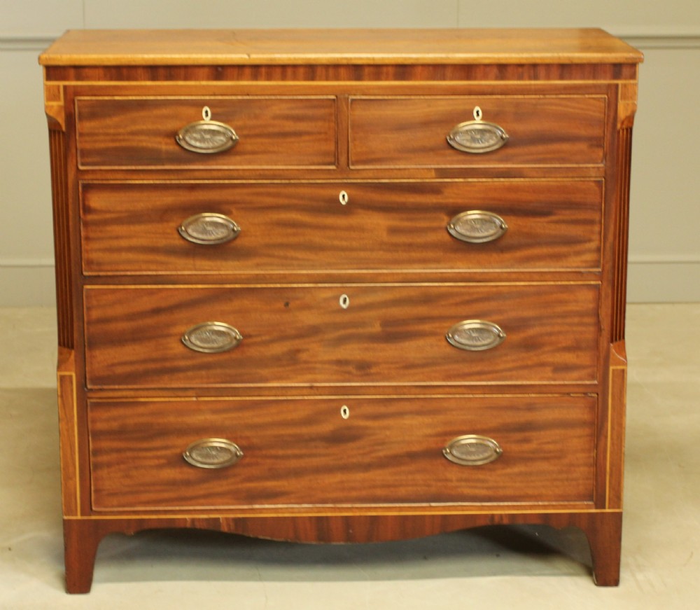 A Victorian flame mahogany chest of drawers featuring boxwood inlay, two short drawers over three long drawers, oval brass handles, and splayed bracket feet.