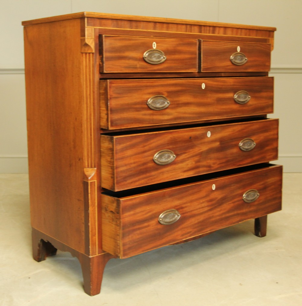 A Victorian flame mahogany chest of drawers featuring boxwood inlay, two short drawers over three long drawers, oval brass handles, and splayed bracket feet. View V