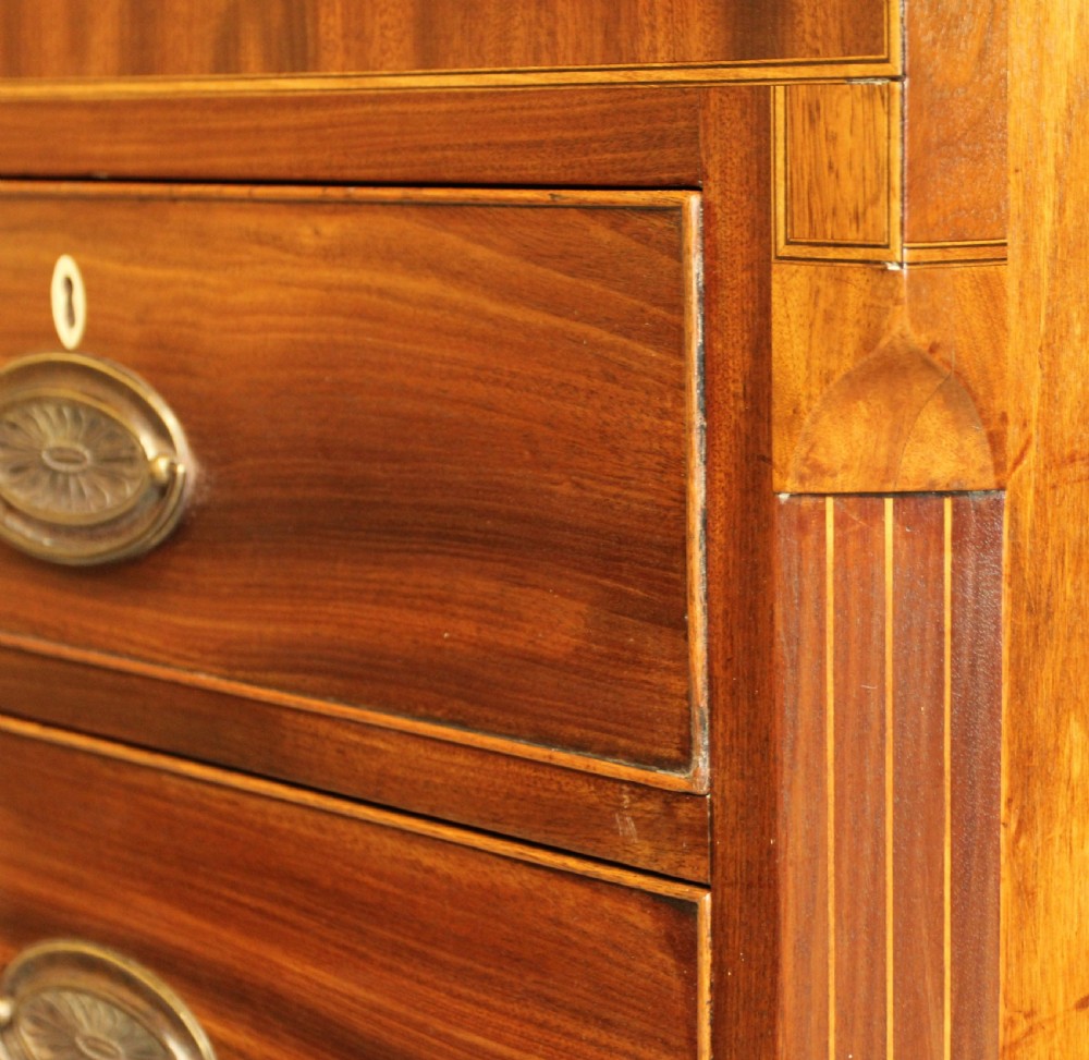 A Victorian flame mahogany chest of drawers featuring boxwood inlay, two short drawers over three long drawers, oval brass handles, and splayed bracket feet. View VI