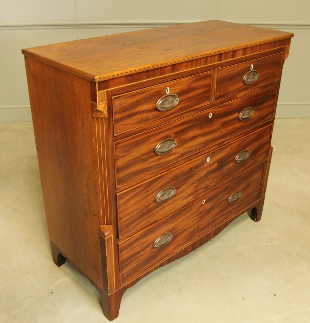 A Victorian flame mahogany chest of drawers featuring boxwood inlay, two short drawers over three long drawers, oval brass handles, and splayed bracket feet. View VIII