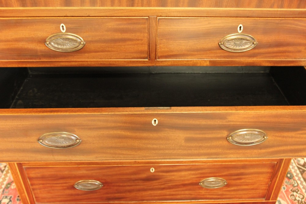 A Victorian flame mahogany chest of drawers featuring boxwood inlay, two short drawers over three long drawers, oval brass handles, and splayed bracket feet. View X