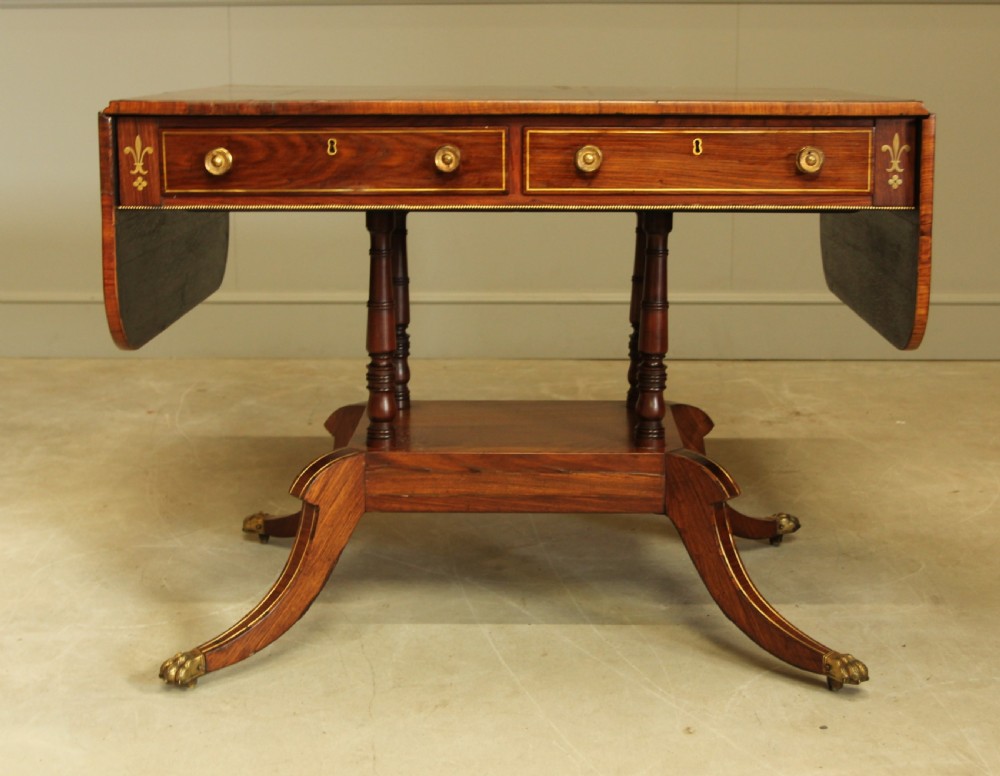 A Regency rosewood sofa table featuring brass stringing inlay, two frieze drawers, twin turned pedestal columns, and splayed legs with brass paw feet. View II