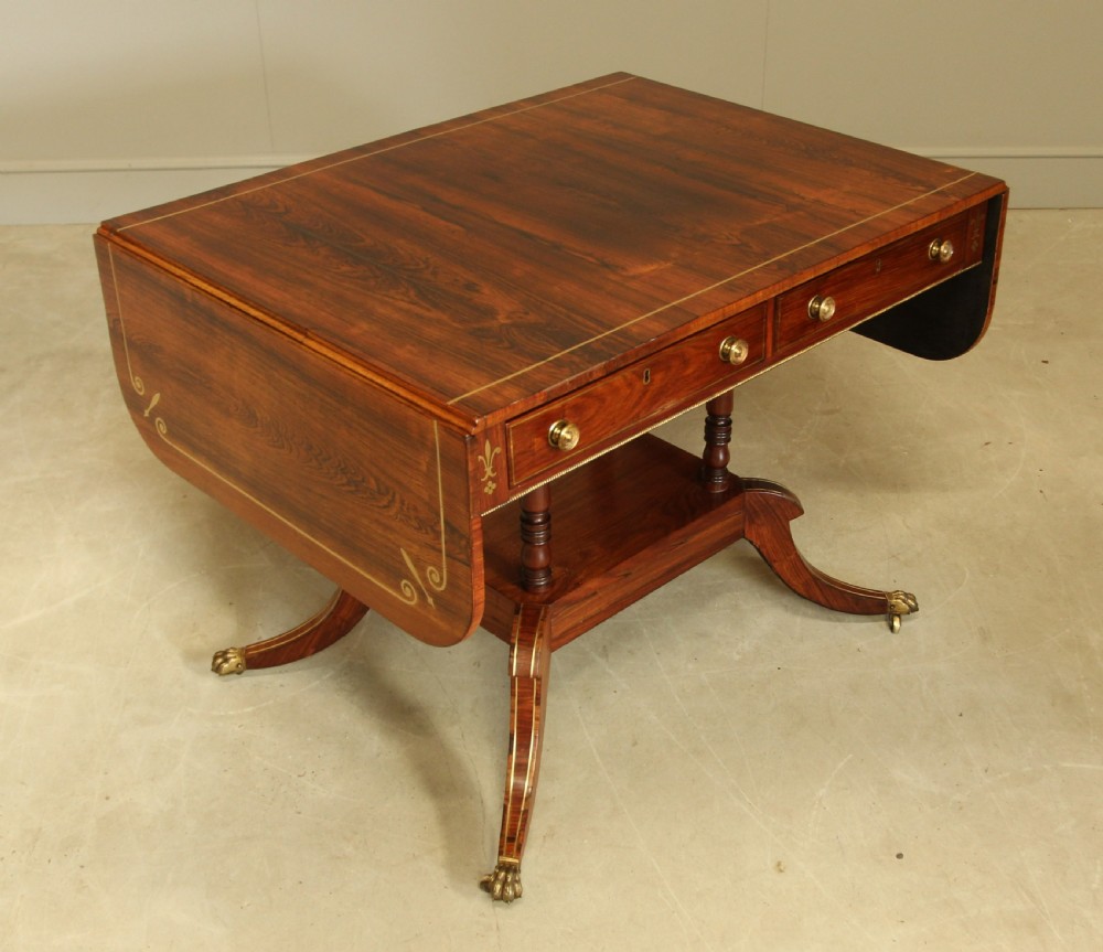 A Regency rosewood sofa table featuring brass stringing inlay, two frieze drawers, twin turned pedestal columns, and splayed legs with brass paw feet. View V