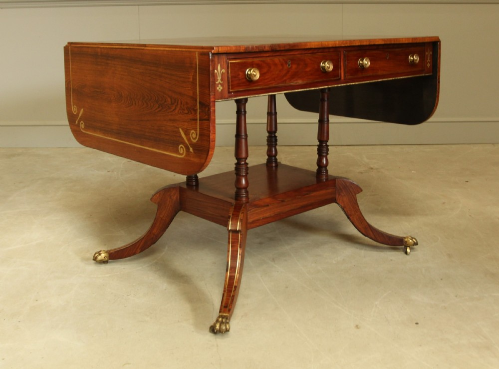 A Regency rosewood sofa table featuring brass stringing inlay, two frieze drawers, twin turned pedestal columns, and splayed legs with brass paw feet. View VI
