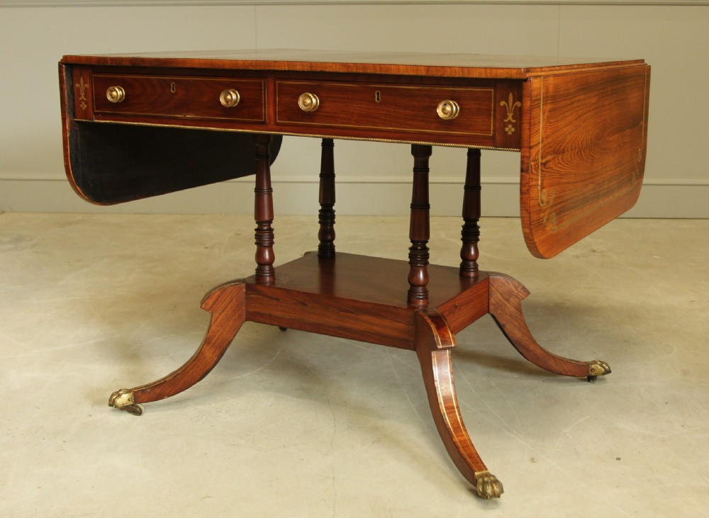 A Regency rosewood sofa table featuring brass stringing inlay, two frieze drawers, twin turned pedestal columns, and splayed legs with brass paw feet. View VII