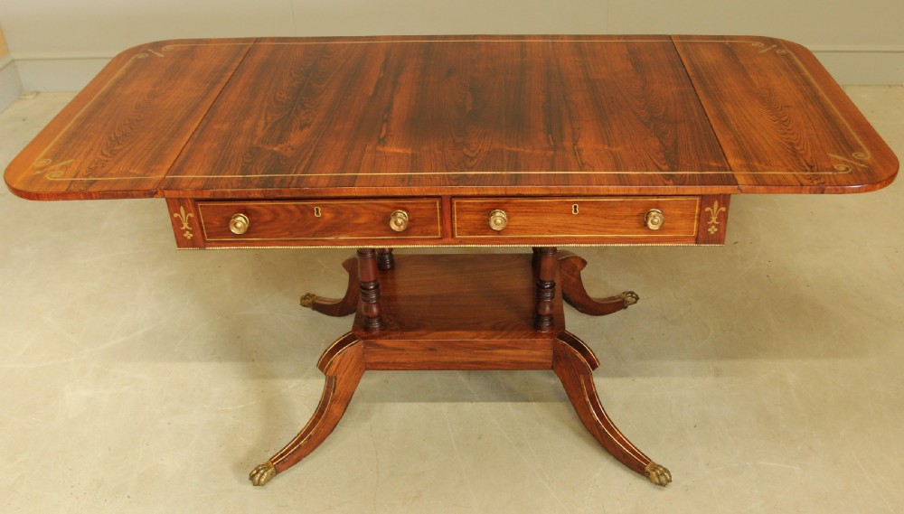 A Regency rosewood sofa table featuring brass stringing inlay, two frieze drawers, twin turned pedestal columns, and splayed legs with brass paw feet. View VIII