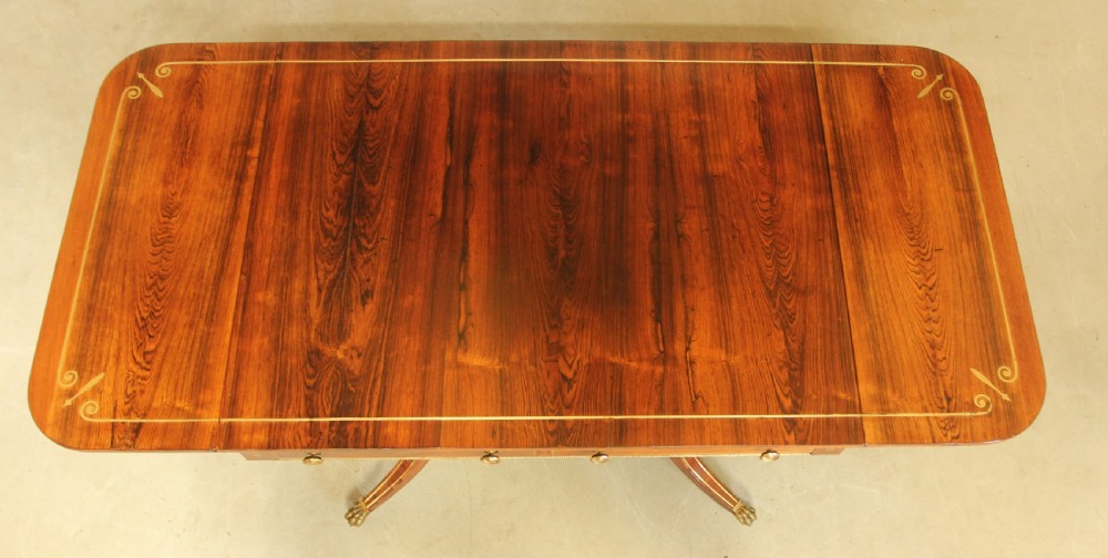 A Regency rosewood sofa table featuring brass stringing inlay, two frieze drawers, twin turned pedestal columns, and splayed legs with brass paw feet. View IX