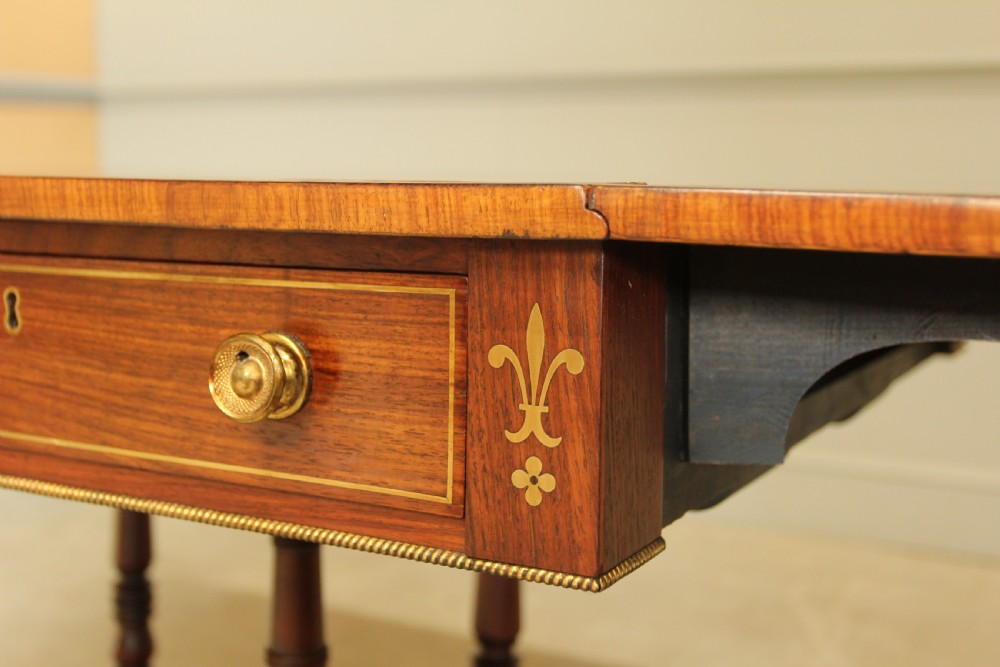 A Regency rosewood sofa table featuring brass stringing inlay, two frieze drawers, twin turned pedestal columns, and splayed legs with brass paw feet. View X