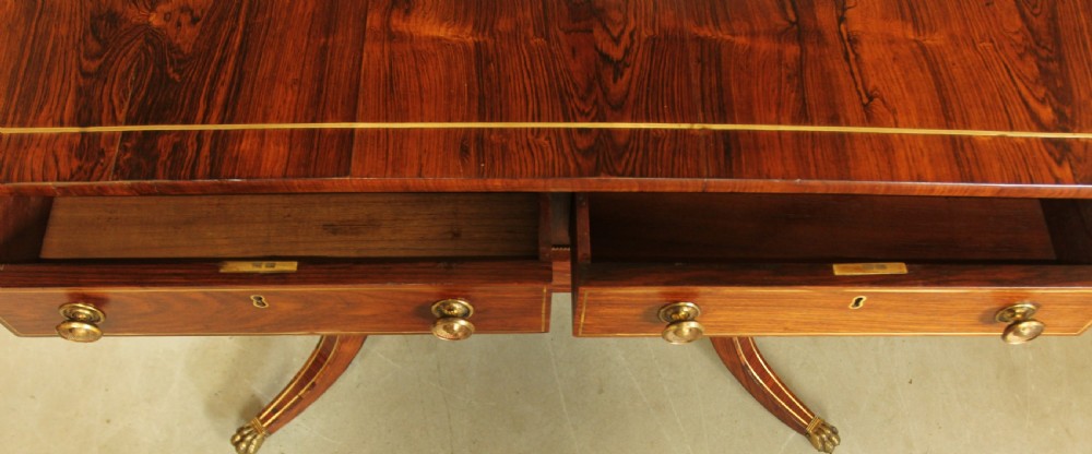 A Regency rosewood sofa table featuring brass stringing inlay, two frieze drawers, twin turned pedestal columns, and splayed legs with brass paw feet. View XI