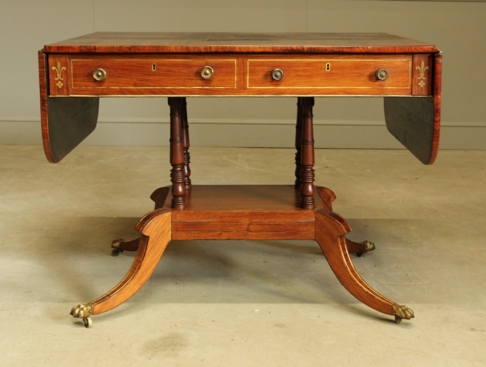 A Regency rosewood sofa table featuring brass stringing inlay, two frieze drawers, twin turned pedestal columns, and splayed legs with brass paw feet. View XIII