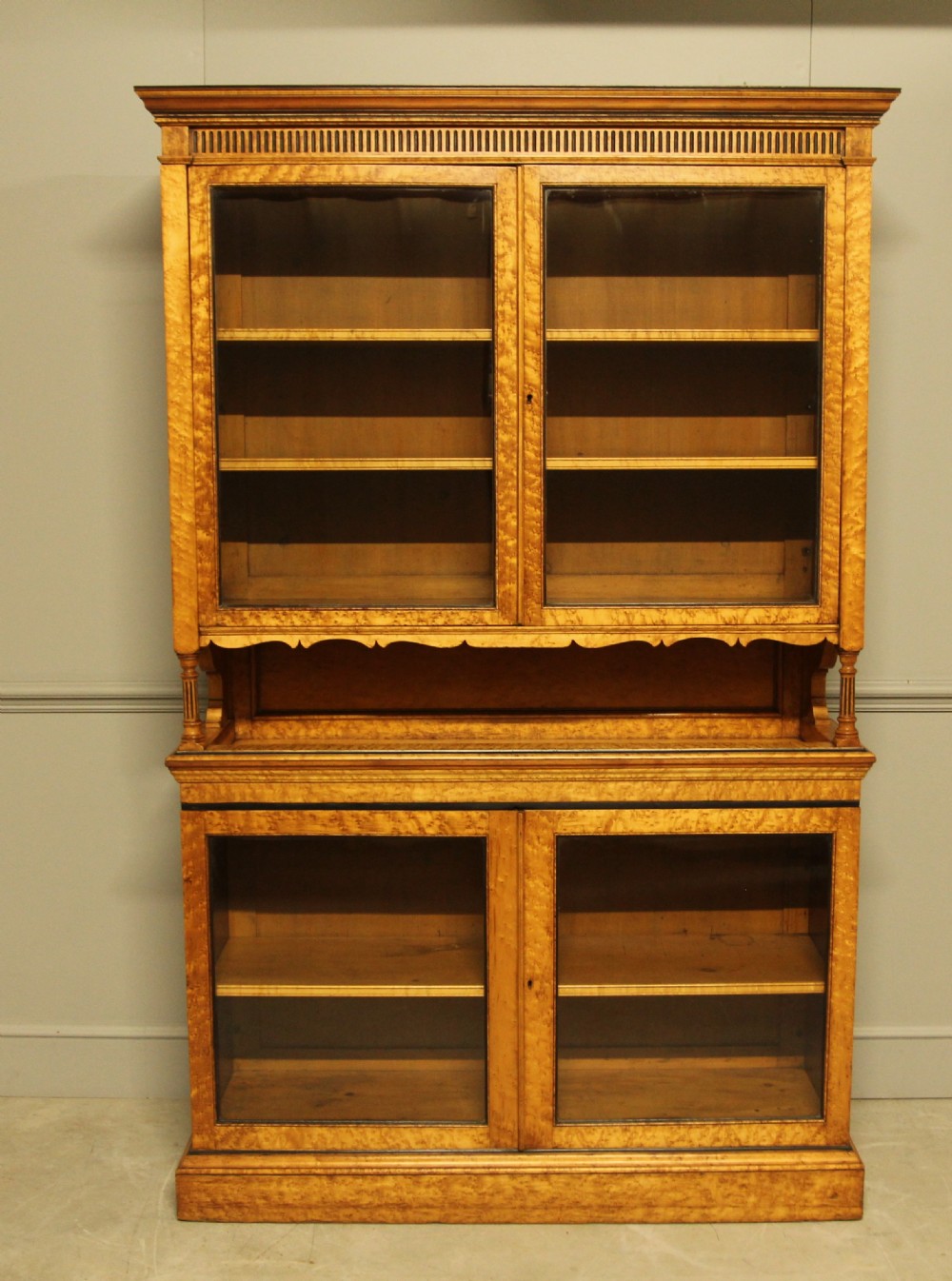 A two-tier Victorian display cabinet crafted from golden birds eye maple veneer with glazed double doors on both the upper and lower sections.