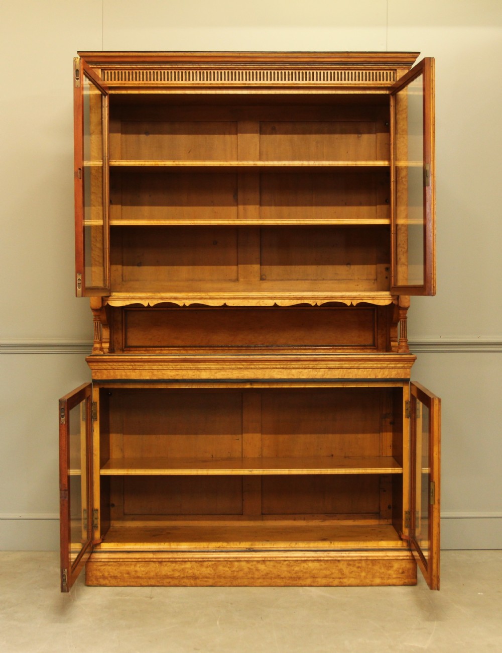 A two-tier Victorian display cabinet crafted from golden birds eye maple veneer with glazed double doors on both the upper and lower sections. View V