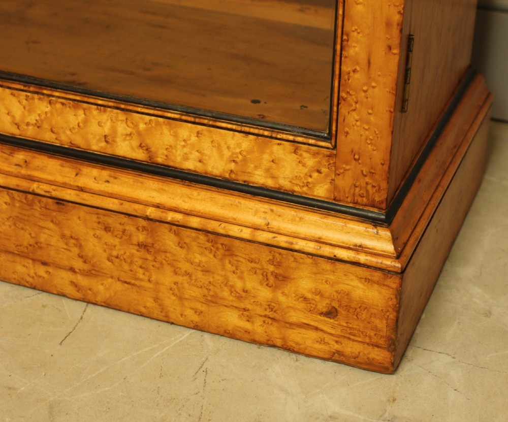 A two-tier Victorian display cabinet crafted from golden birds eye maple veneer with glazed double doors on both the upper and lower sections. View X
