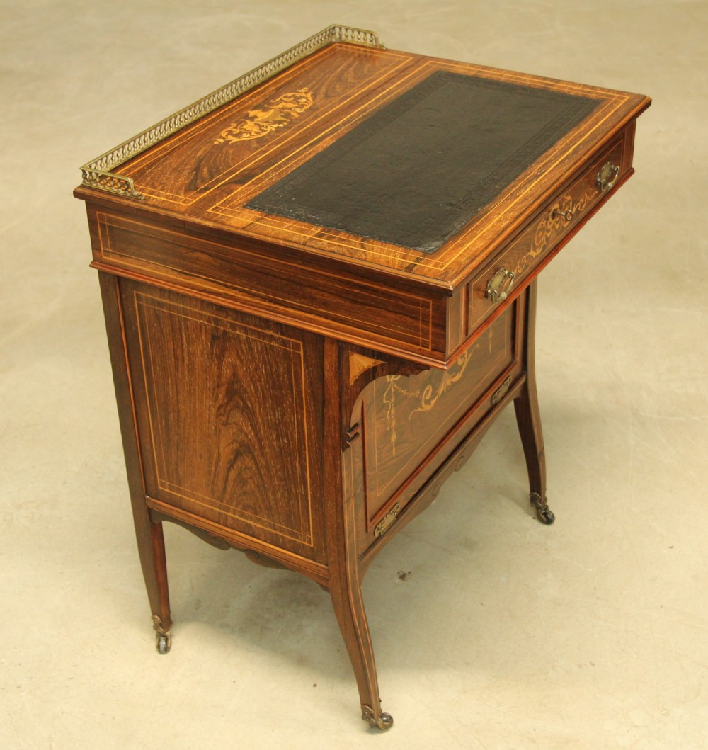 A Victorian rosewood Davenport desk featuring fine floral marquetry inlay, a black leather writing surface, a brass gallery rail, and slender tapered legs on brass castors.