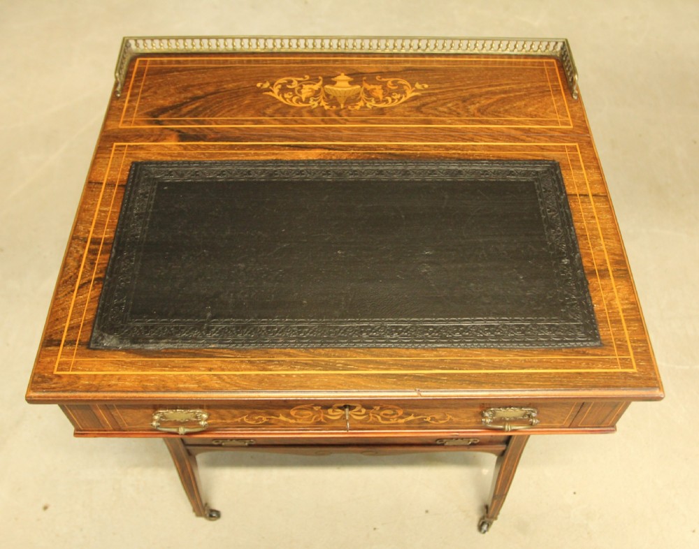 A Victorian rosewood Davenport desk featuring fine floral marquetry inlay, a black leather writing surface, a brass gallery rail, and slender tapered legs on brass castors. View V