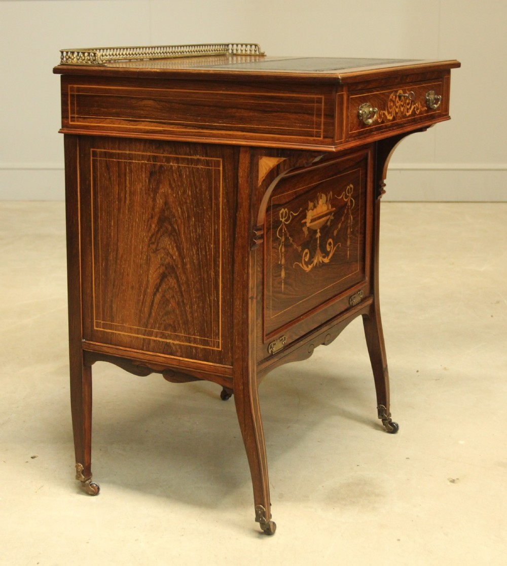 A Victorian rosewood Davenport desk featuring fine floral marquetry inlay, a black leather writing surface, a brass gallery rail, and slender tapered legs on brass castors. View VI