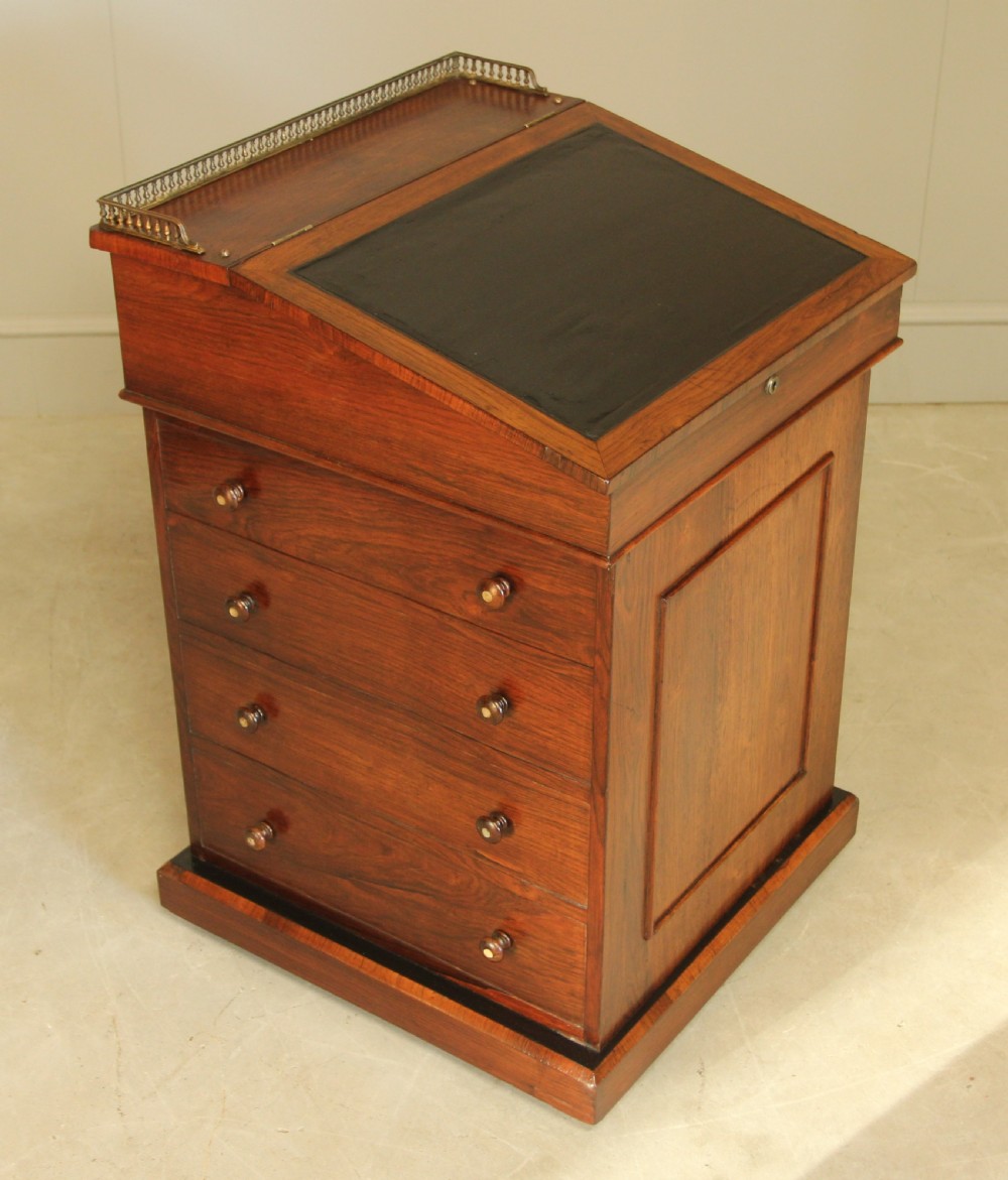 An early 19th-century rosewood Davenport desk featuring a slanted leather-inset writing surface, brass top gallery rail, and side drawers.