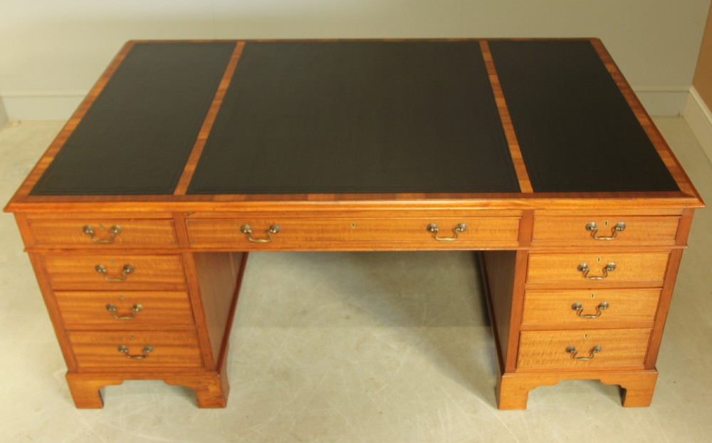 An early 20th-century mahogany partners desk featuring a dark leather writing surface, multiple drawers with brass swan-neck handles, and twin pedestals on bracket feet. View II