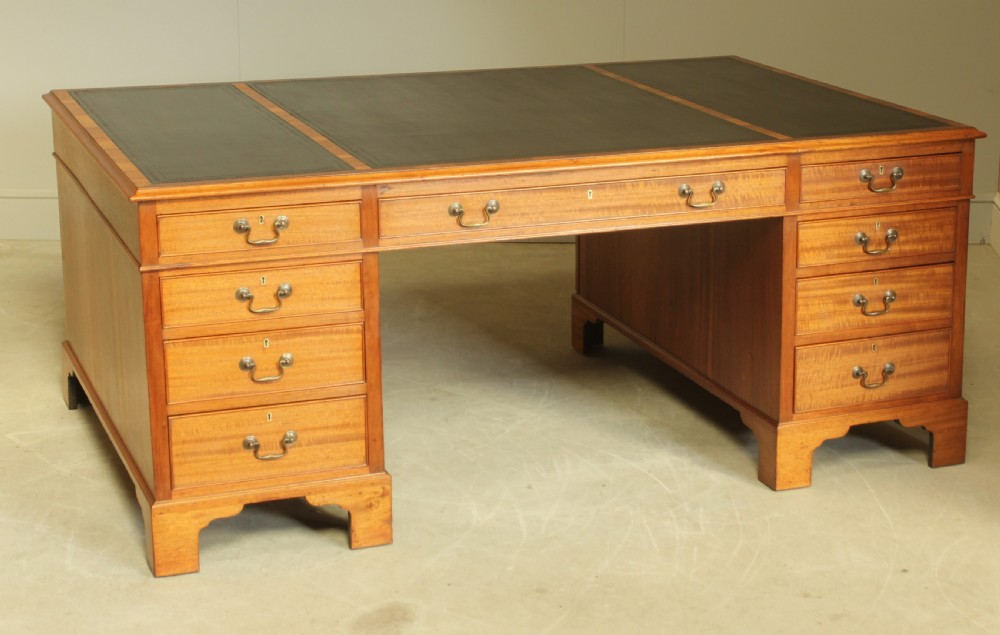An early 20th-century mahogany partners desk featuring a dark leather writing surface, multiple drawers with brass swan-neck handles, and twin pedestals on bracket feet. View III
