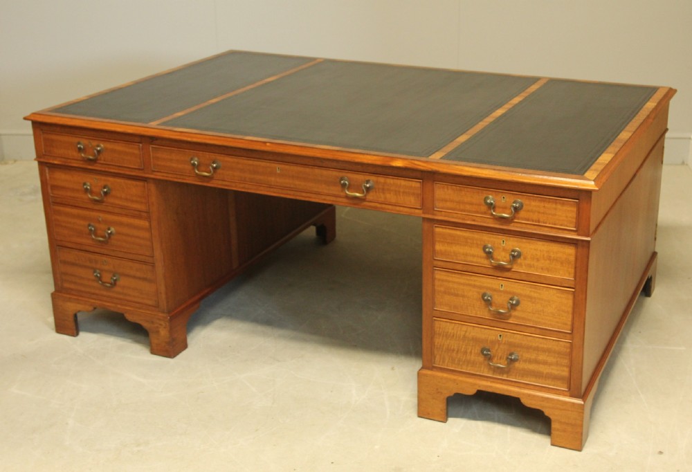 An early 20th-century mahogany partners desk featuring a dark leather writing surface, multiple drawers with brass swan-neck handles, and twin pedestals on bracket feet. View V